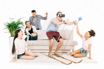 smiling young multiethnic friends looking at young man in virtual reality headset skiing isolated on / Photodune, Misc