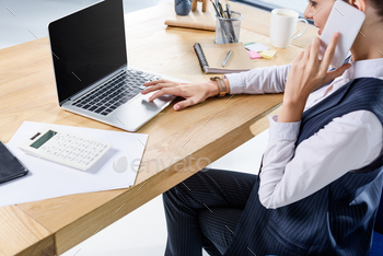 Young businesswoman sitting in office at her desk, talking on phone and using her laptop / Photodune, Misc