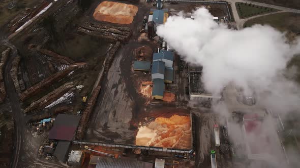 Revealing Top Down Shot of Operating Log Sawmill Factory with Large Chimney Emitting Smoke Aerial