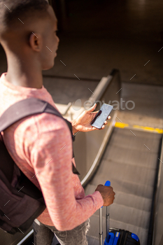 behind young black man going down escalator with suitcase and mobile phone in hand / Photodune, Misc