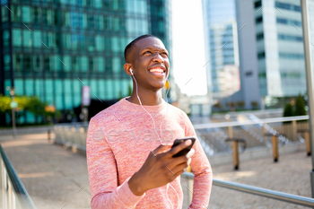 cheerful young black man using phone and listening to music with earphones in city / Photodune, Misc