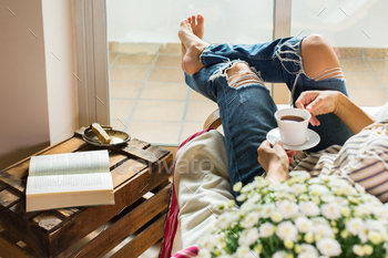 Young woman is relaxing at home, drinking tea, reading book / Photodune, Misc