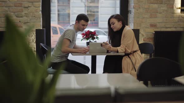 Side View Portrait of Happy Millennial Caucasian Couple Surfing Internet on Tablet and Talking in