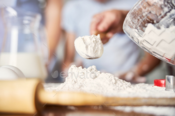 Baker tipping wooden spoon full of flour on table surface / Photodune, Misc