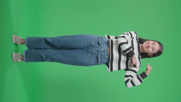 Full Body Of A Smiling Asian Woman Pointing Bicep While Standing In Front Of Green Screen Background