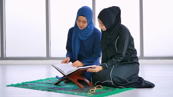 Two Muslim Asian women wearing traditional hijab are reciting prayers in the Quran.