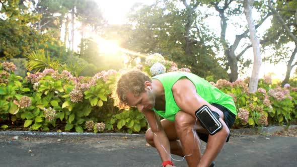 Man tying his shoe laces while jogging in park