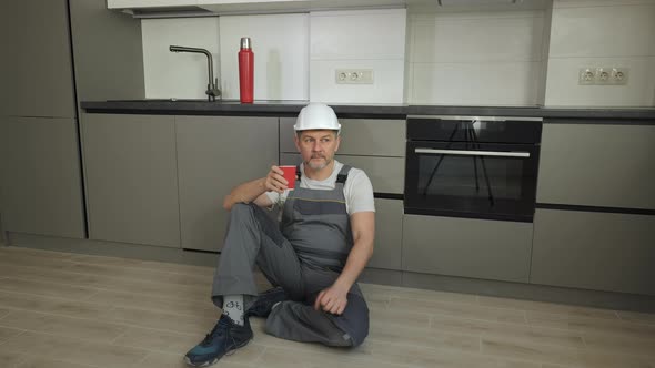 The Worker Sits on the Floor Resting and Drinking Tea in the New Kitchen