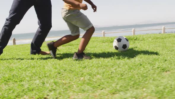 Video of legs of african american father and son playing soccer outdoors and having fun