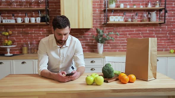 Man Browsing on Mobile Phone at Home Kitchen. Handsome Young Man Browsing on Smartphone Smiling