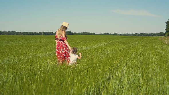 Slow Motion Young Mother in Red Dress Which Flutters in Wind Walks Along the Endless Field