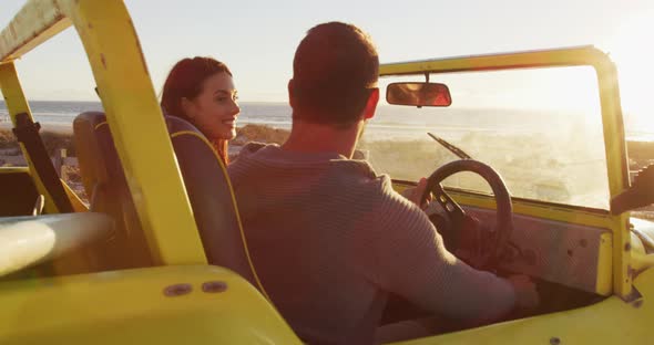 Happy caucasian couple sitting in beach buggy by the sea talking