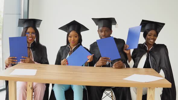 Four Graduates of an African American University or College Sit at a Desk and Show Their Blue
