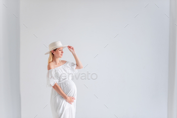 Young pregnant woman in anticipation of baby in white hat, dress, hugs belly. Happy maternity / Photodune, Misc