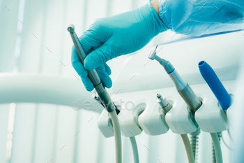 a dentist wearing gloves in the dental office holds a tool before working / Photodune, Misc