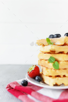Stack of Belgian waffles, blueberry, strawberry cuts, mint leaf, sugar powder / Photodune, Misc