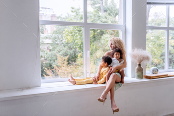 Happy family is sitting on wide windowsill, looking out the window. Single Parenting. Adoption / Photodune, Misc