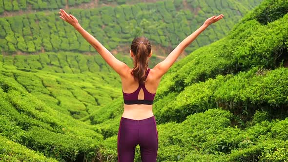 Back View of Young Woman Doing Yoga Poses and Breathing in Tea Plantation in Kerela Munnar