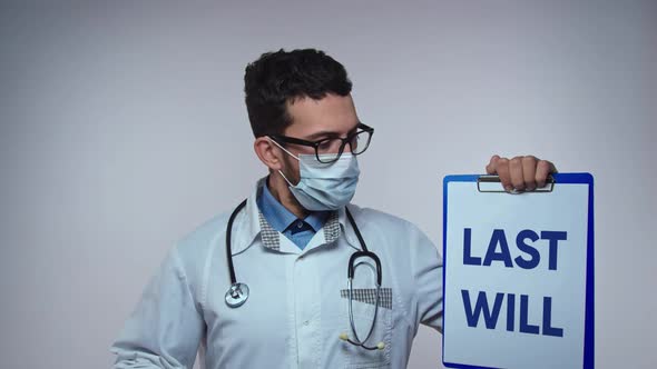 A Medical Professional Wearing a Stethoscope and Protective Face Mask Holds Up a Clipboard with a