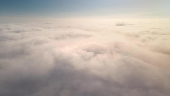 Aerial shot of flying over a layer of soft clouds at dawn