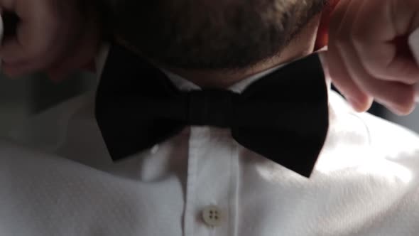 Man Adjusts His Bowtie in a White Shirt.