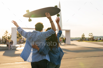 Happy couple enjoy sunset embrace with arms raised hold longboard. Happiness and freedom concept / Photodune, Misc