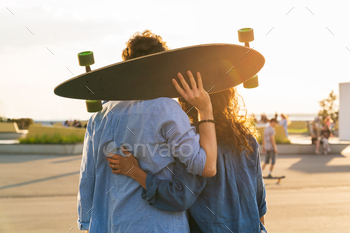 Romantic couple of skateboarders enjoy sunset embracing with longboard in hands in urban skate park / Photodune, Misc