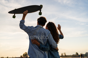 Stylish young couple hug looking at sunset hold skateboard. Happy girl and guy in love enjoy freedom / Photodune, Misc