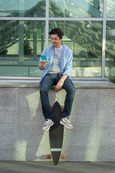 Hipster skater man using smartphone hold longboard in hand reading messages in mobile phone online / Photodune, Misc