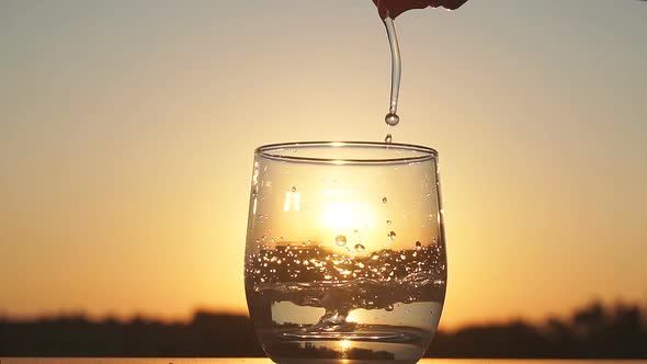 Clean Water Is Poured Into a Glass at Sunset