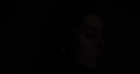 Female Face On A Black Background. Appears And Plunges Into Darkness Again.