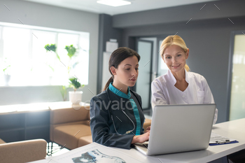 Young female intern and blond doctor searching information in internet / Photodune, Misc