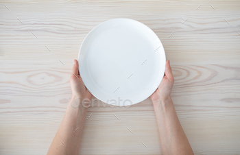 Woman holding empty plate waiting for food, sitting on wooden table, top view, copy space / Photodune, Misc