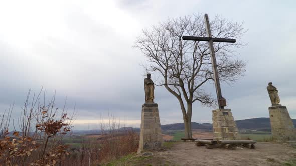 A Historic Sacred Site with Two Statues and a Wooden Cross Set in Nature.