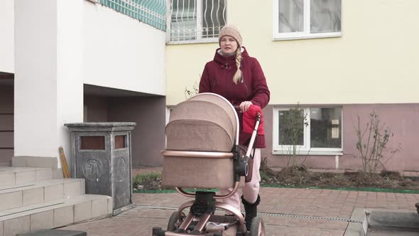 A girl Walks with a Child and a Pram Down the Street