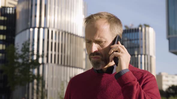 A Middleaged Handsome Caucasian Man Talks on a Smartphone Upset in an Urban Area