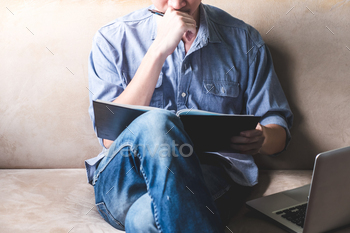Casual young man reading documents on sofa at home.