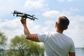 A man with a flying vehicle in his hands, raised to the sky in nature.Launching a drone / Photodune, Misc