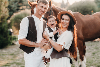 A family in white clothes with their son stand near two beautiful horses in nature. A stylish couple / Photodune, Misc