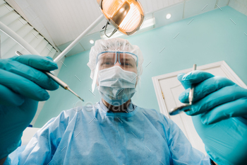 a dentist wearing a protective mask sits nearby and holds instruments in his hands before treating a / Photodune, Misc