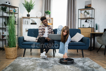 Couple using laptop and robot vacuum cleaner for household / Photodune, Misc