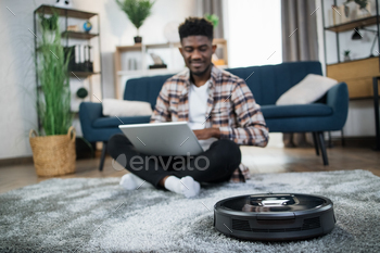 Positive african guy using robotic vacuum cleaner for chores / Photodune, Misc