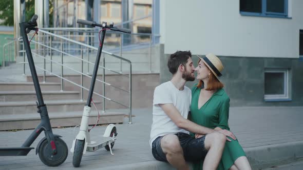 Couple in Love Sitting on Pavement at Scooters Admires and Kisses Each Other