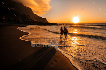 A couple in love stands in the ocean in the evening looking at the beautiful sunset on the island of / Photodune, Misc