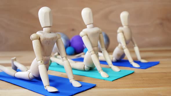 Wooden figurine exercising on exercise mat in front of gym balls against wooden background