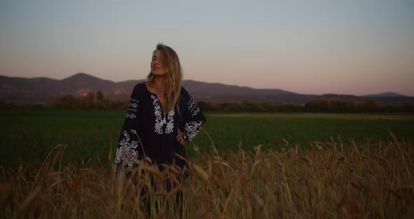 Young woman in national Ukrainian clothes standing on a field of wheat at sunset or sunrise