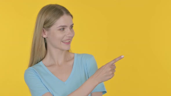 Young Woman Pointing on Side on Yellow Background