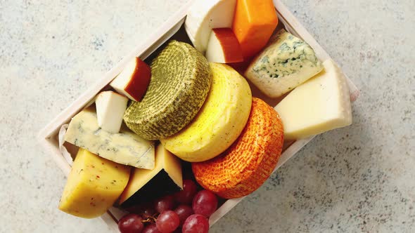 Fresh and Delicious Different Kinds of Cheeses Placed in Wooden Crate with Grapes