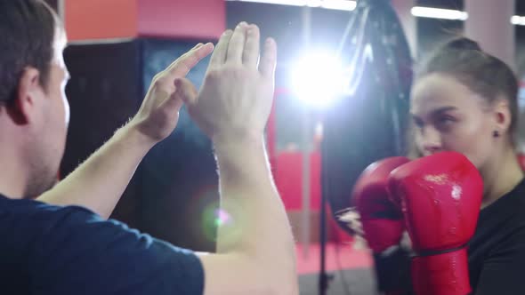 A Young Pretty Woman Trains Her Punch at the Hands of Her Boxing Coach