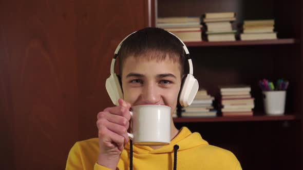 Happy young man student in white wireless headphones drinks from a white mug 